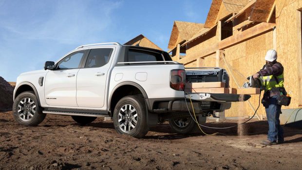 A Ford Ranger Wildtrak poke-in hybrid ute offering AC energy for instruments on an city worksite with a tradesman in physique