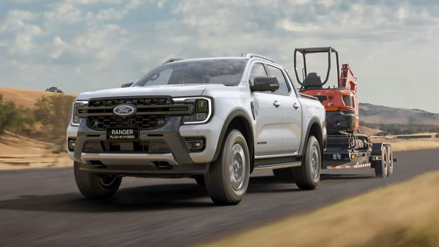 A Ford Ranger Wildtrak plug-in hybrid ute driving down a rustic avenue while towing a portion of commercial machinery