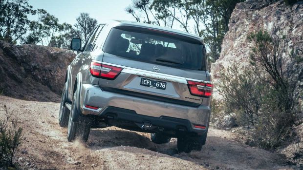 Rear spy of a 2023 Nissan Patrol Warrior ascending a hill on a gravel road